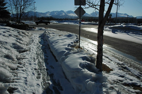 Breakup, sidewalk footprints in the ice and melting snow, pickup truck, signs, Chugach Range, Anchorage, Alaska by Wonderlane