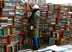 Photograph of a man standing in front of overflowing book shelves in open market
