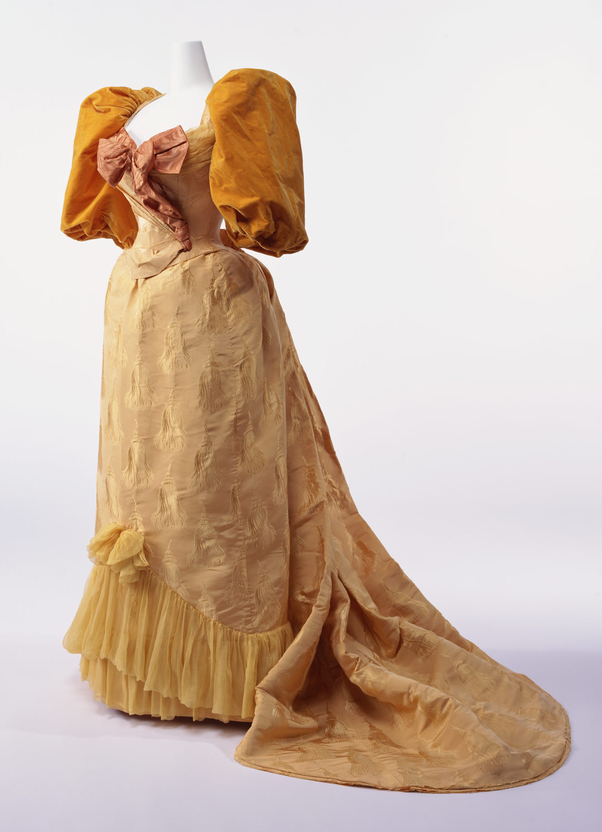 1894. Ball Gown. silk brocade with tassel pattern; two-piece dress with gigot sleeves; silk taffeta bow at breast; silk chiffon decoration at hem of skirt. Credit KCI