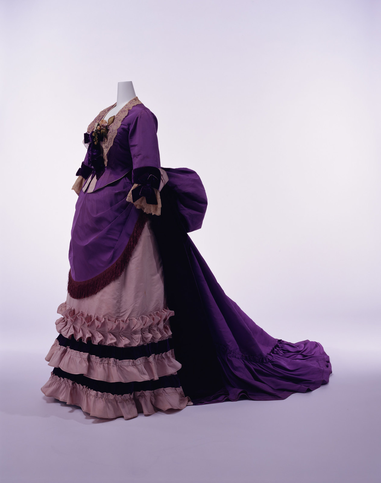 1894. Afternoon Dress. Silk faille set of bodice and skirt; silk lace and velvet bows at neck and cuffs; apron-shaped overskirt with silk fringe at front. Credit KCI