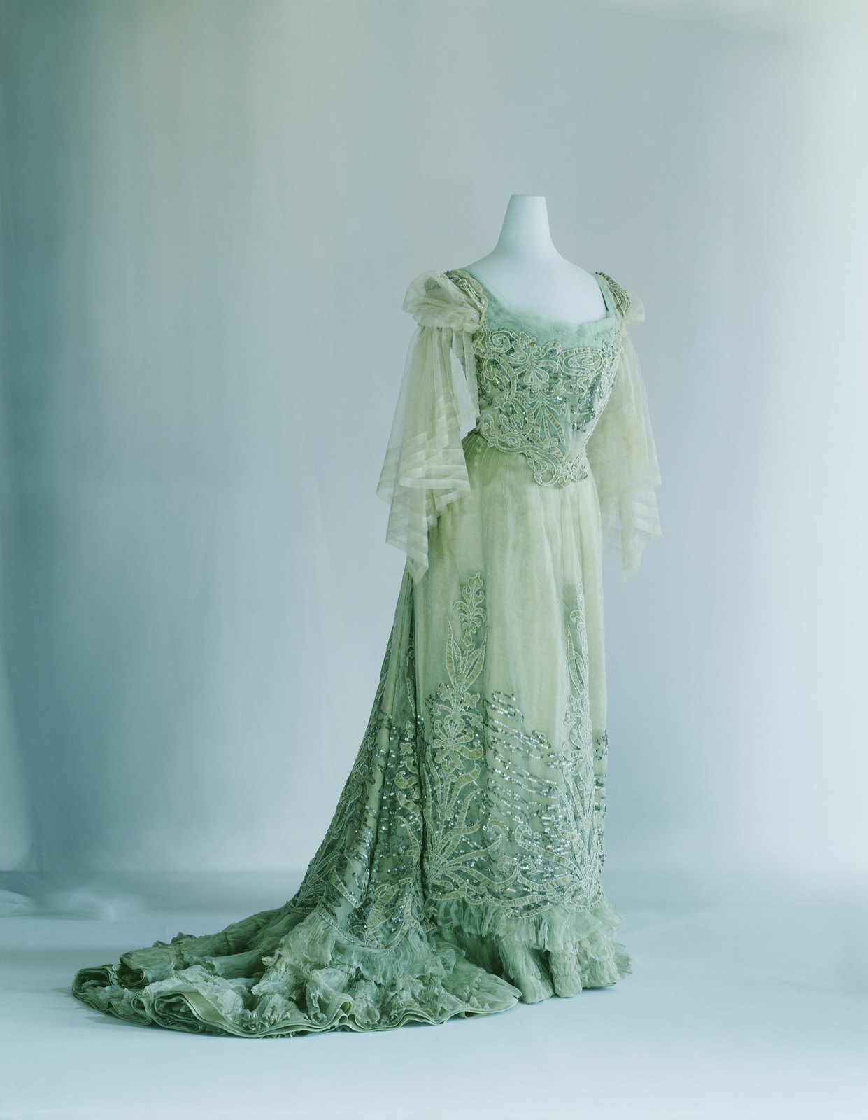 1900. Evening Dress. Pale green silk chiffon and velvet; S-curve silhouette; appliqué of plant pattern; sequin and cord embroidery with water's-edge pattern. Credit KCI