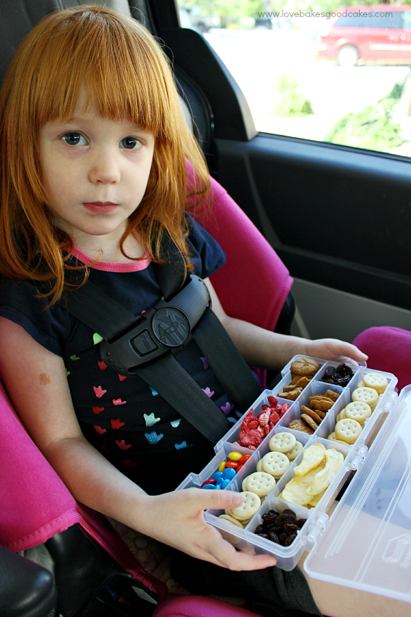 A girl holding a plastic box with snacks inside.