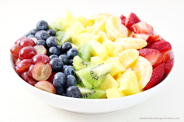 Rainbow Fruit Salad with Honey Citrus Dressing in a white bowl close up.