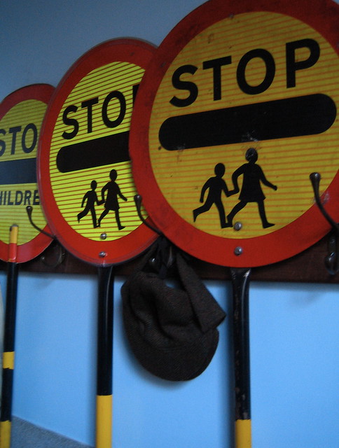 Three round signs with a yellow background bordered in red saying Stop with a black bar underneath. The leftmost says children underneath while the other two have graphics of two children running.