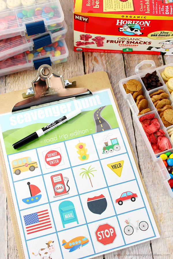 Road Trip Scavenger Hunt Printable on a clipboard with a pen and snacks.