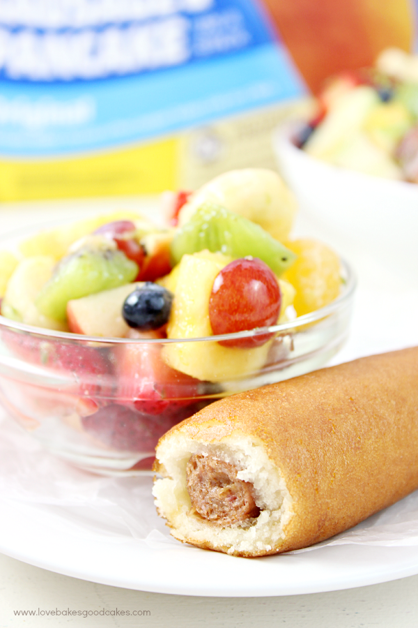 Rainbow Fruit Salad with Honey Citrus Dressing in a clear bowl with a corn dog.