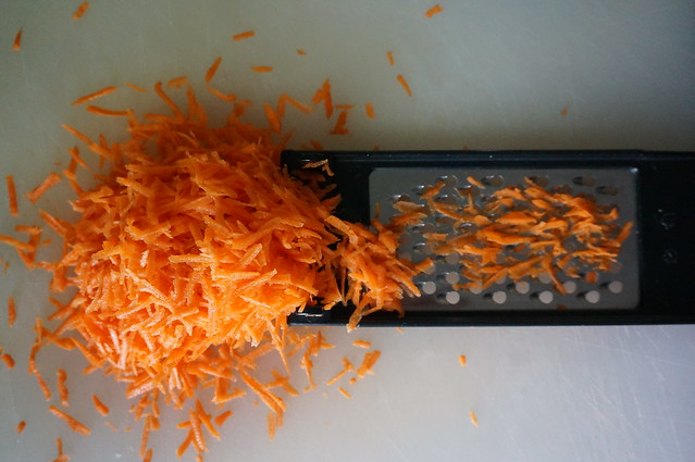 A pile of shredded carrots spilling onto a flat grater. They are shocking vibrant.