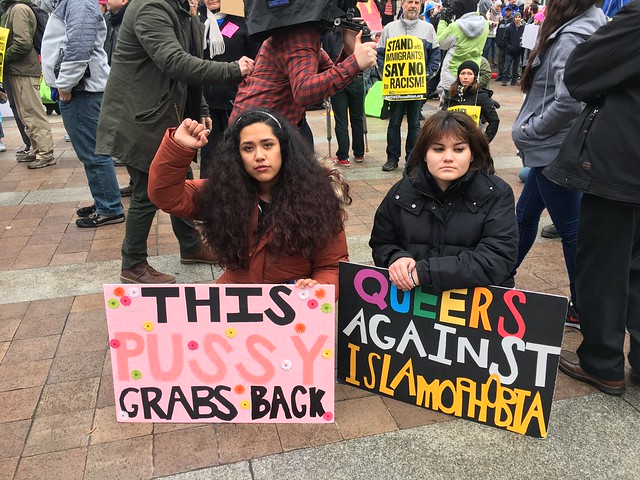 Alena Chavez and Raini Vargas hold signs and kneel while the national anthem is played while participating in the ANSWER Coalition protest.