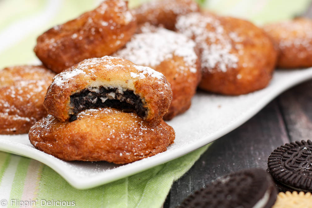 gluten free deep fried oreo cookie dusted in powdered sugar on a white plate beside some gluten free sandwich cookies