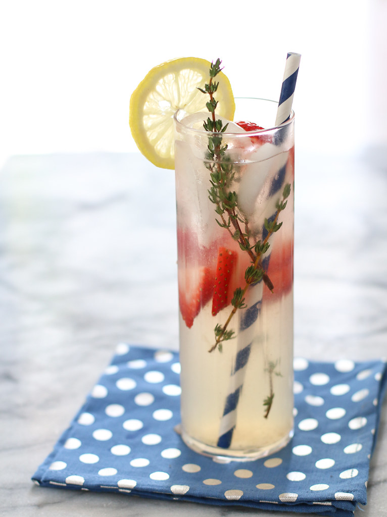 strawberry thyme lemonade with straw in a tall glass on polka dot napkin