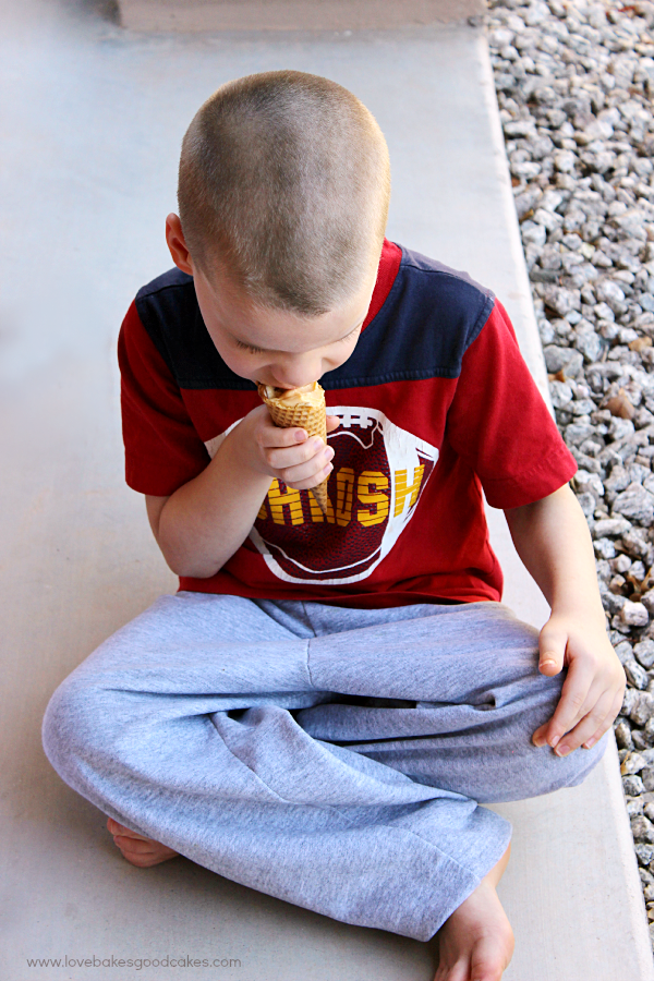 A boy sitting down eating an ice cream cone.