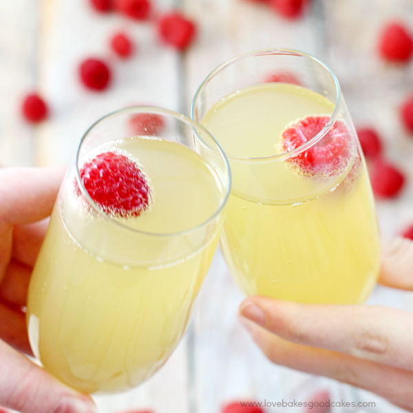 Mock Champagne Punch in two glasses toasting each other with fresh raspberries.