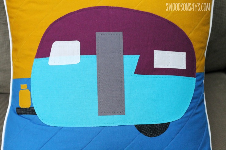 A camper applique on a quilted pillow background.