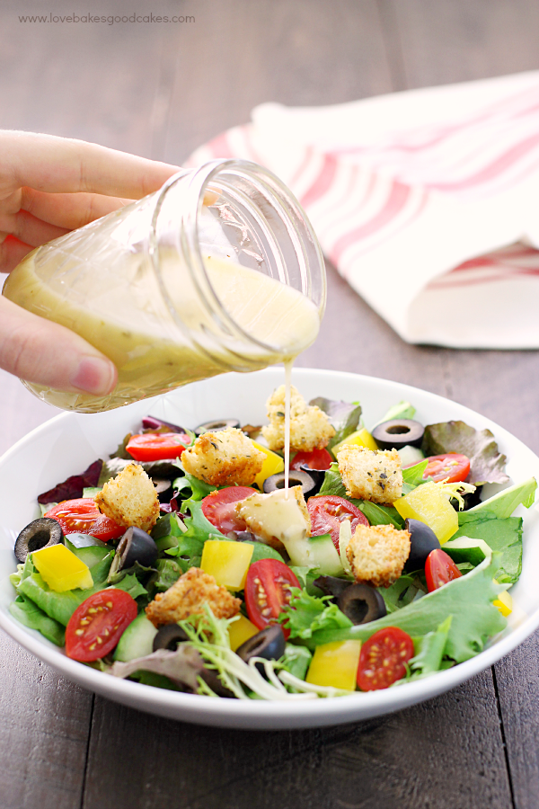 Italian-Style Salad in a bowl with Italian dressing being poured over the top.