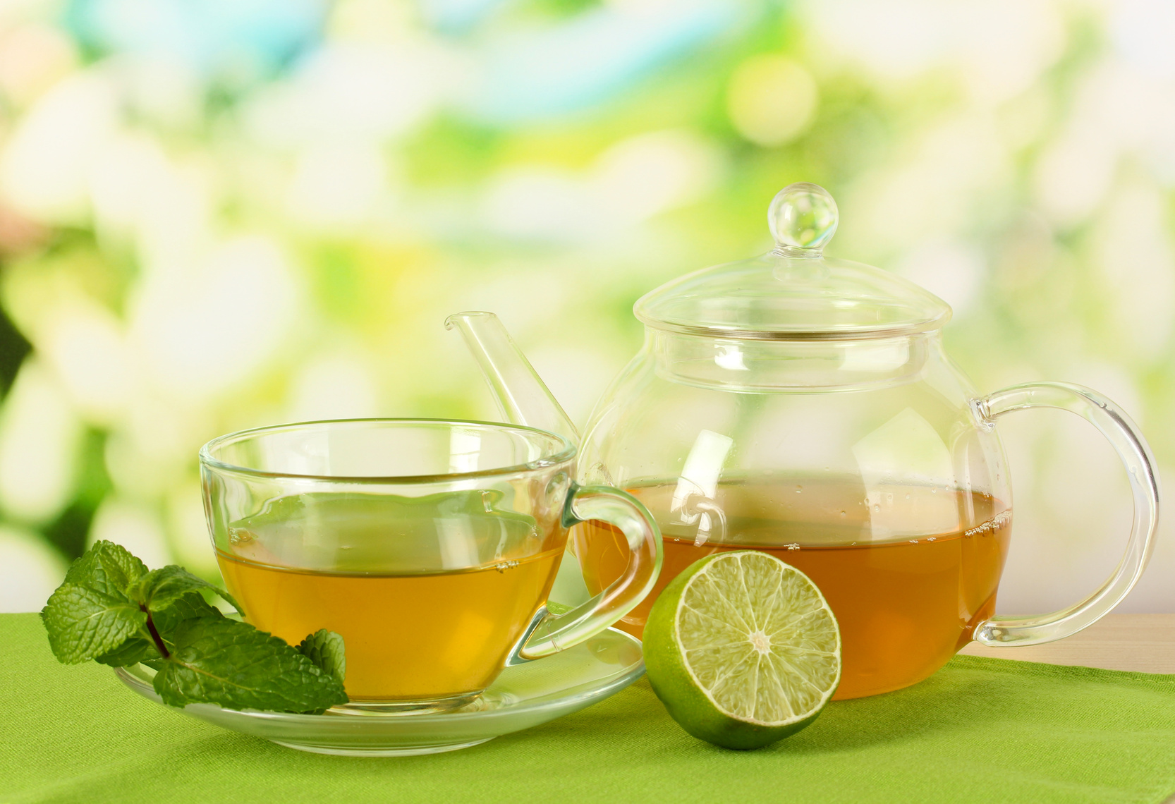 Cup of tea with mint and lime on table on bright background