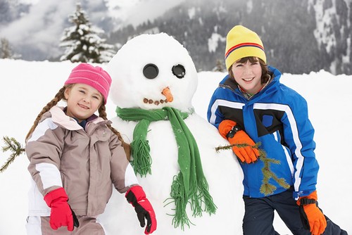 Two Young Children Building Snowman On Ski Holiday In Mountains