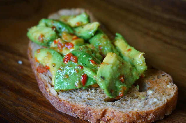 Avocado toast: spicy edition. A close-up shot looking down a long slice of avocado toast, colored and flecked by bright red bits of spicy chili paste
