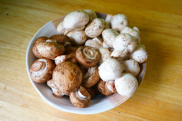 Brown crimini mushrooms and white button mushrooms sit, divided, in a bowl that is itself divded into almost the exact same colors. It's like this two-tone bowl was made for these two-tone mushrooms.