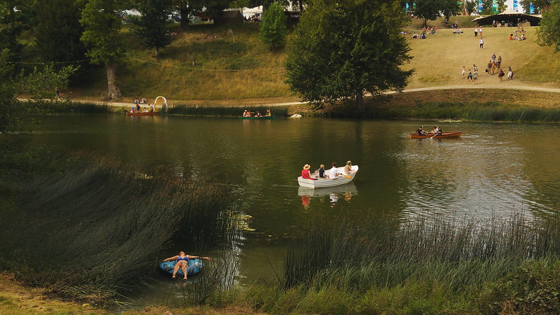 People in boats on a calm lake with a grassy verge behind