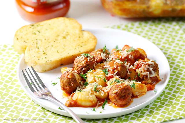 Gnocchi and Meatball Bake on a white plate with garlic bread and a fork.
