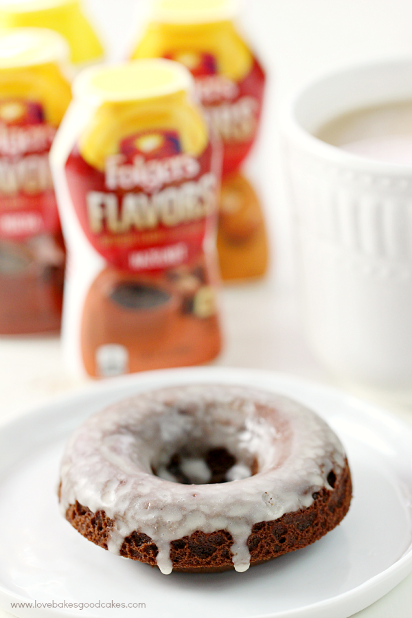 Glazed Chocolate Donut on a plate with Folgers Flavors in the background and a cup of coffee.