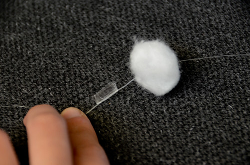 4: Once finished threading, for each cotton ball, wrap a piece of double-sided tape where you want the ball to sit