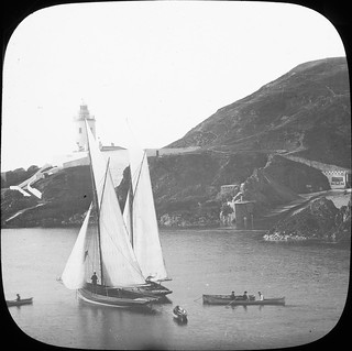 Sloops at anchor in harbour, lighthouse on outcrop in distance