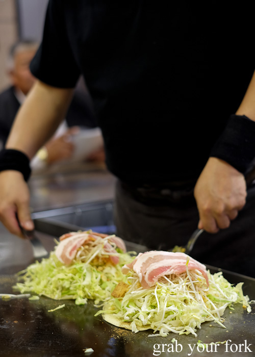 Adding bacon rashers to our Hiroshima-style okonomiyaki at Okonomimura, Hiroshima