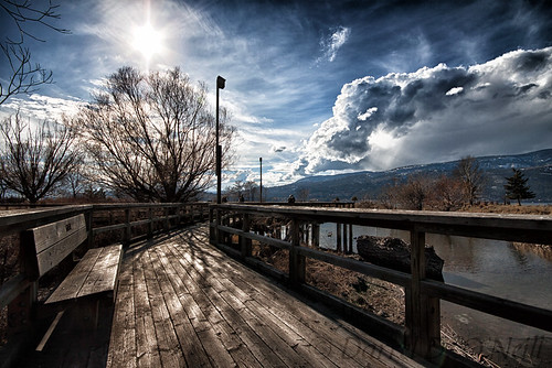 landscape scenic boardwalk water pond wetland trees sky cloud sun mountains hills bench railing park birdhouse white blue brown nature kelowna bc canada okanagan person people lake forest