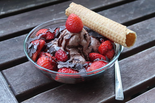 Nuss-Nougat-Eis mit frischen Erdbeeren, Schokoladensoße, Schokoraspeln und Waffelröllchen