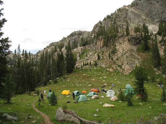 tents in a green valley surrounded by rocky mountains and alpine trees and people getting up in the morning along the beartooth highway