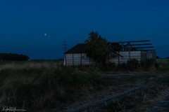 Rising blood moon eclipse over over a dilapidated barn