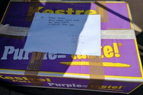A purple fresh produce box made for potatoes, taped up with postal details on a piece of paper attached to the top