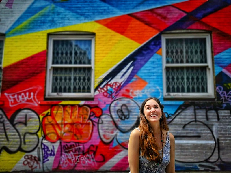Flora smiling in front of bright jagged graffiti in Shoreditch