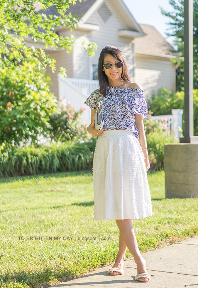 one shoulder floral top, gold jewelry, blue gray clutch, white clip dot midi skirt, white sandals with fringe