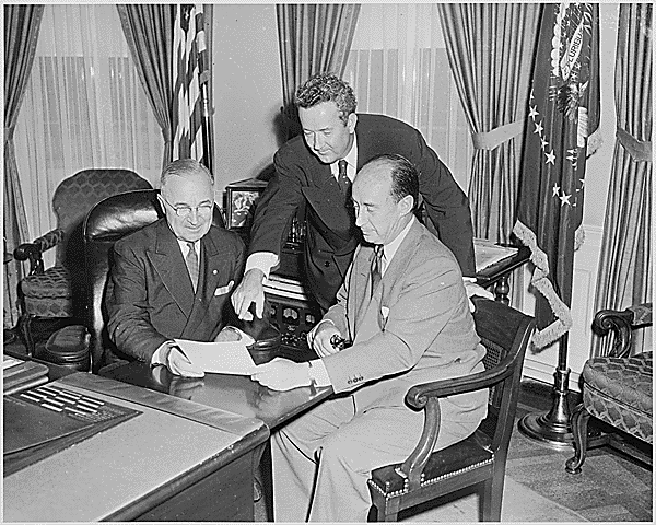 U.S. President Harry Truman (left), Democratic presidential candidate Adlai Stevenson (right), and Democratic vice presidential candidate John Sparkman (standing) meeting in the Oval Office on August 12, 1952. Photo from the holdings of the National Archives and Records Administration, cataloged under the National Archives Identifier (NAID) 200393. 